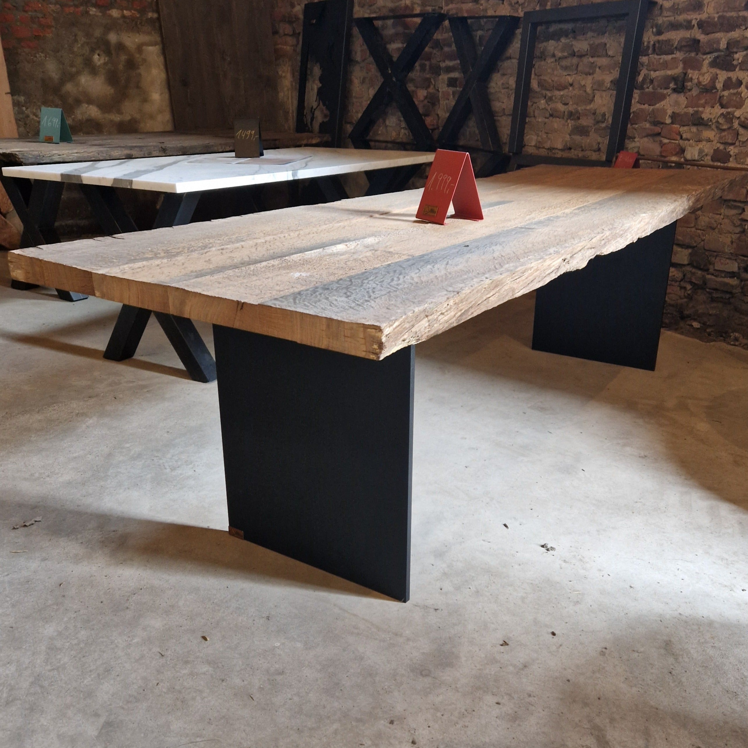 Im Vordergrund ein massiver Tisch mit gebürsteter Eichenplatte und schwarzen Stahlwangen als Beine, dahinter weitere Tische.