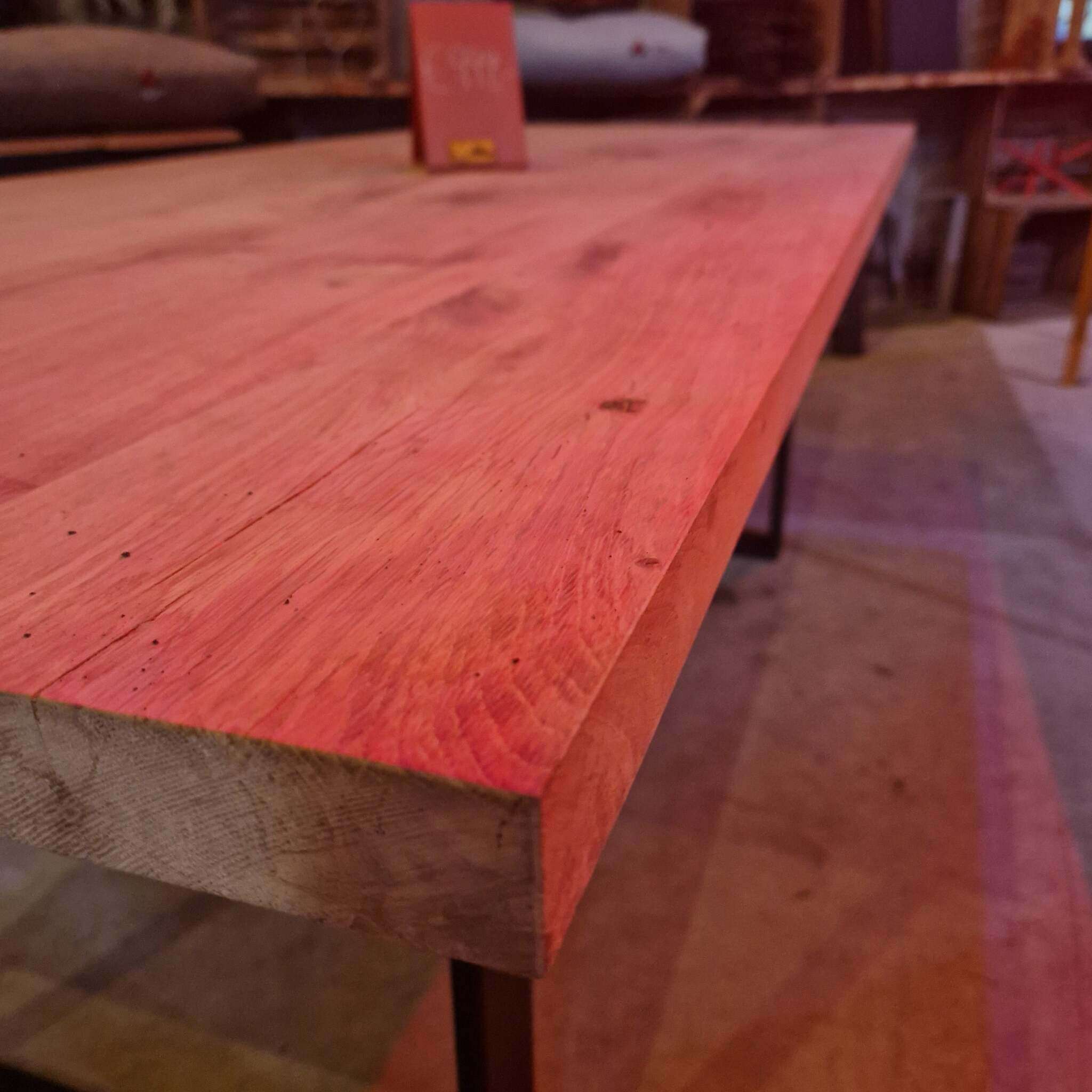 Ein massiver Holztisch mit gehobelter Eichenplatte in Nahaufnahme, markante Maserung, Metallbeine, im rustikalen Innenraum.